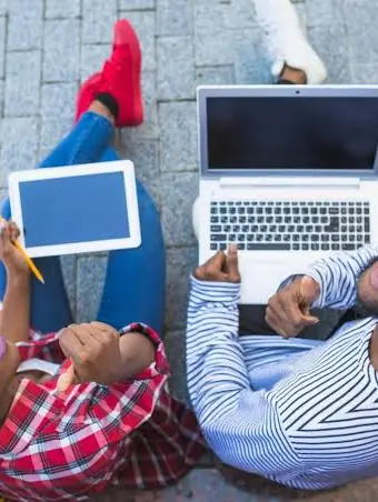 Two students smiling up from their laptop and tablet